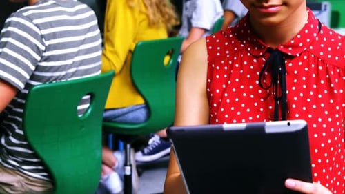 Schulmädchen nutzt digitales Tablet, während andere Schüler im Klassenzimmer am Computer lernen