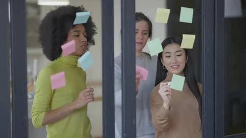 Plan du milieu de trois jeunes femmes multiethniques concentrées qui collent des notes sur une conversation en miroir