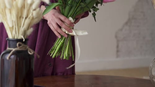 Une fleuriste met un bouquet fini sur la table.