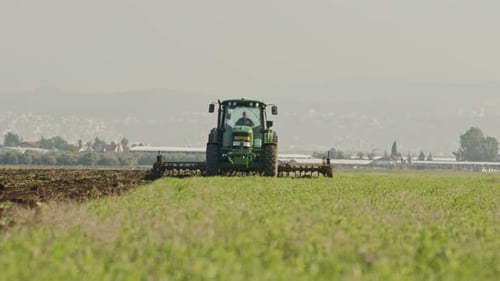 Tractor cultivating a green field in slow motion.