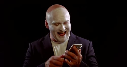 Verrückter Mann mit weißer Fettfarbe im Gesicht lacht und tippt auf dem Smartphone