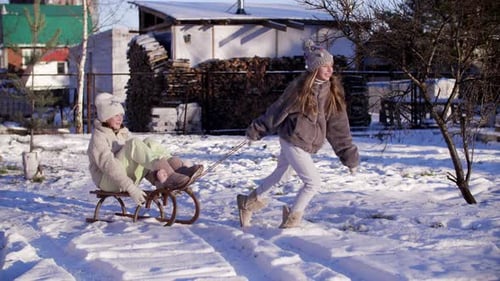 Playful Girl Riding Girlfriend on Sledge on Snowy Countryside on Holiday Vacations. Laughing