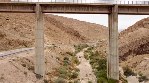 aerial forward drone shot,ing slowly under an empty train bridge, revealing an empty road, dry strea