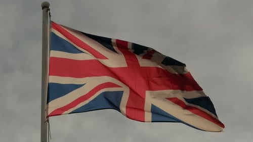 Tattered United Kingdom Flag Flapping Against Cloudy Sky