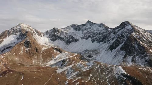 Berggipfel mit Schneeflecken und weißen Wolken vor klarem Himmel