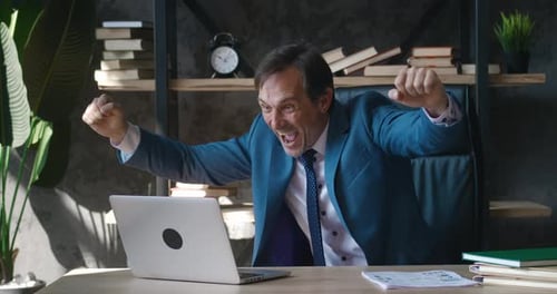 Excited businessman celebrates success with laptop at desk