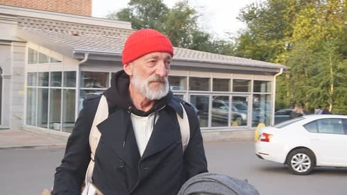 Man Walking in Urban Setting With Red Cap