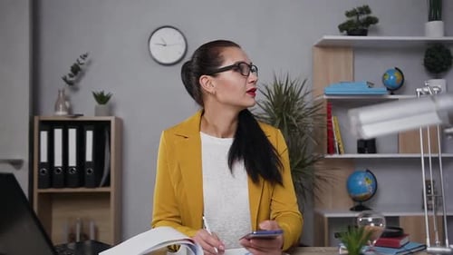 Arbeiterin in Brille, die zur Seite schaut und sich dann Notizen macht, um mit Diagrammen zu berichten