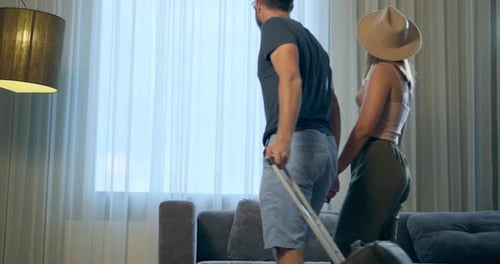 Un couple avec une valise entre dans la chambre et s'assoit sur le canapé