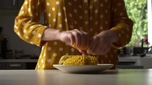 femme frotte du sel sur du maïs à la cuisine