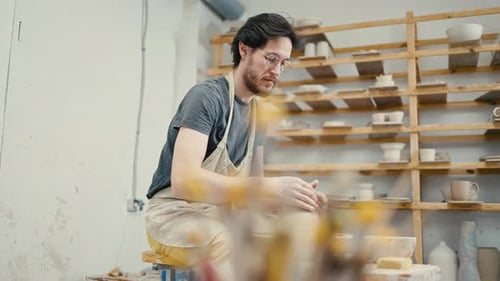 Tracking-Aufnahme eines männlichen Töpfers, der an der Töpferscheibe arbeitet und Keramikgeschirr in Zeitlupe formt
