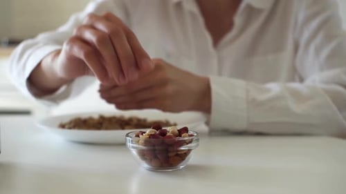 Close Up Girl's Hands Are Peeling Peanuts. Peanut Shelling. Nuts In A Plate A White Race Girl Sits