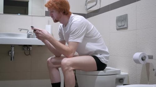 Redhead Man Using Smartphone in Toilet Commode
