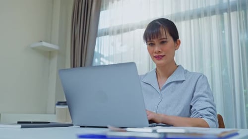Asian attractive happy business woman sit on working table, turn on laptop computer in office.