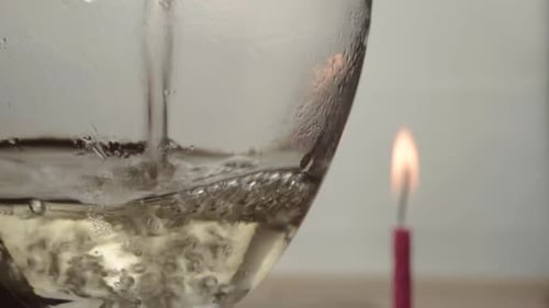 Pouring glass of white wine with candle in background close up shot