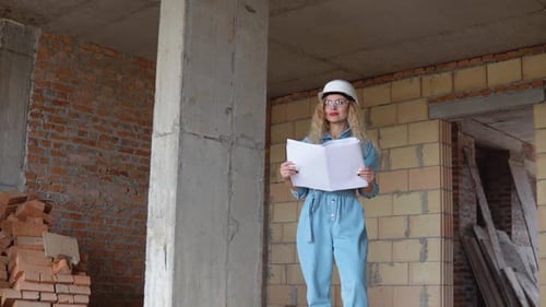Eine junge Frau mit weißem Arbeitshelm, Jeansoverall und Schutzbrille steht auf der Baustelle