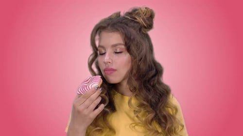 Young Woman Eating Donut on Pink and Green Backdrop