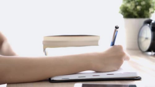 Woman Writing in Notebook at Desk with Pen