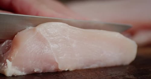 Männerhände mit Messer schneiden rohes Hähnchenfilet in Stücke.