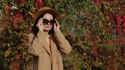 Stylish Woman Puts on Sunglasses in Autumn Sunlight