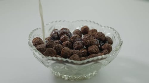 Milk being poured over chocolate cereal in bowl