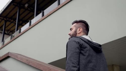 Stylish Brunet Adult Guy in Grey Hoodie Walking Up Stairs in a Restaurant