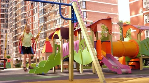A Little Happy Boy Rides on a Swing on a Modern Playground in the Courtyard