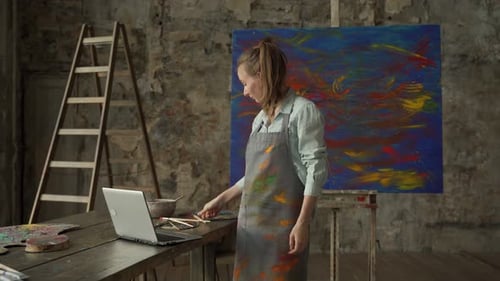 Young Woman Artist Online in Studio with Laptop