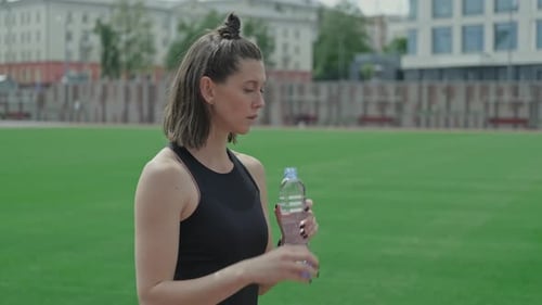 Young Athletic Woman Drinking Water From Bottle at Stadium After Training.