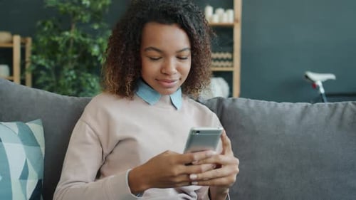 Young Afro-American Woman Enjoying Social Media on Smartphone in Modern Apartment