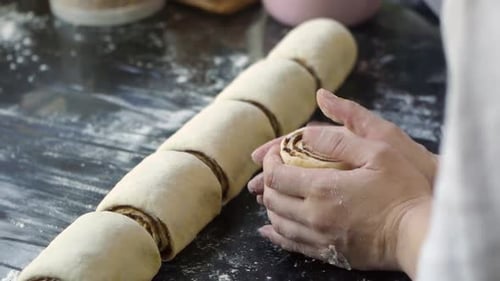 Freshly rolled and cut cinnamon roll dough shaped by fingers in preparation for baking on kitchen ta