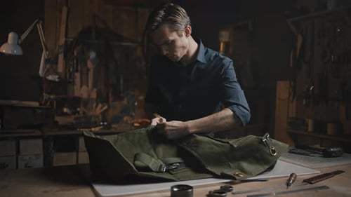 Young Man Tailor Unpicking Canvas Produkt bei der Werkstatt Vorbereitung von Stoffen für die Wiederverwendung am Abend Tracking