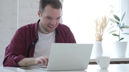 Man Celebrates Success Looking at Laptop at Home