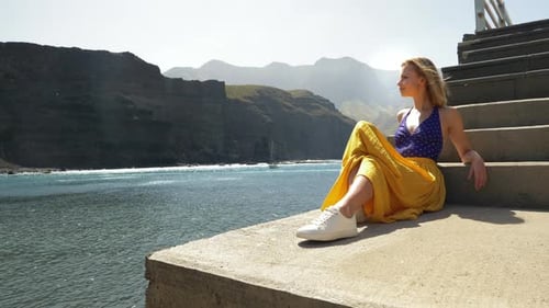 Woman Sitting on Steps Overlooking Ocean and Mountains