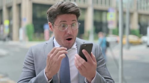 Middle Aged Businessman Reacting to Loss on on Smartphone