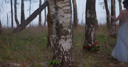 Eine Braut in einem grauen Kleid geht mit einem Hochzeitsstrauß im Wald spazieren