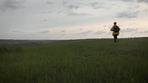 Person Walks Through Green Field on Cloudy Day
