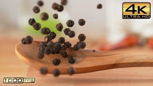 Black peppercorns falling onto a wooden spoon