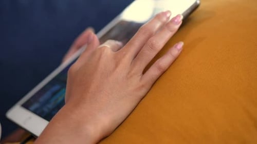 Feche a mão de uma jovem asiática enquanto está no sofá usando um tablet.