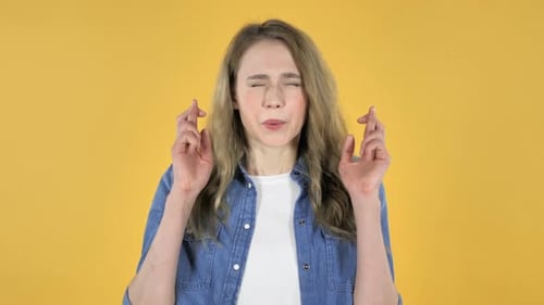Woman Wishing and Crossing Fingers on Yellow Background