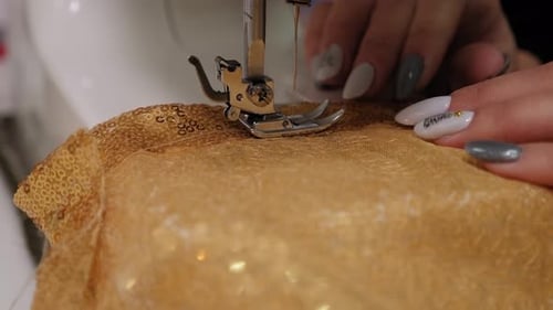 Costureira costurando um vestido feito de tecido dourado perfurado em uma máquina de costura
