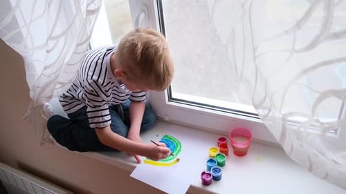 Boy Painting a Colorful Rainbow on Window Sill