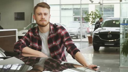 Young Handsome Man Showing Car Keys To His New Auto at the Dealership Salon