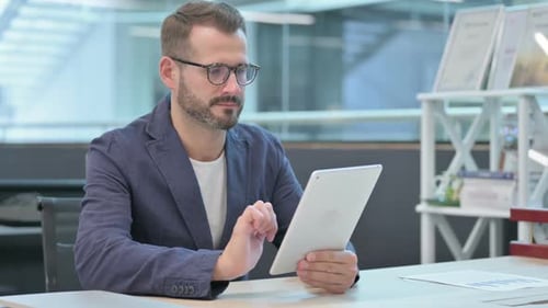 Middle Aged Businessman Browsing Internet on Tablet While Sitting in Office