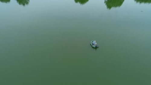 Aerial View Fisherman is Fishing Sitting on an Inflatable Boat in Middle of Lake