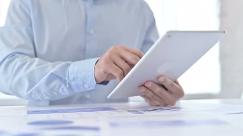 Nahaufnahme der Hände eines jungen Mannes bei der Arbeit an Dokumenten und Tablets