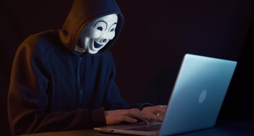 Mysterious Masked Hacker Typing on Laptop in Dark Room