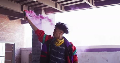 Mixed race man holding purple flare standing in an empty building