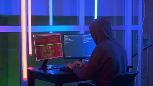 Vue arrière d'un hacker habillé dans le noir travaillant sur un ordinateur