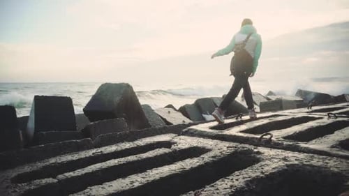 Attractive Young Woman in a Warm Jacket Walking on the Stone Beach at Sunset